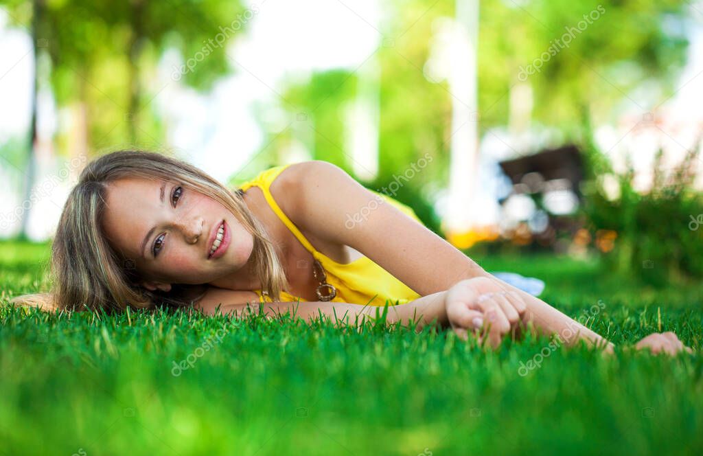 Close up portrait of a young girl lying on green grass, summer park outdoors  