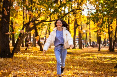 Sonbahar yaprakları dökülüyor. Parkta koşan mutlu genç kız.