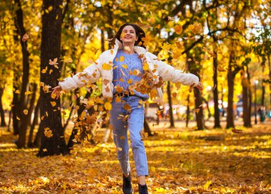 Sonbahar yaprakları dökülüyor. Parkta koşan mutlu genç kız.