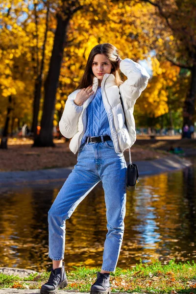一个穿着羊毛衫和蓝色牛仔裤的小女孩在秋天的公园里摆姿势的全长肖像 — 图库照片