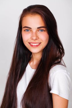 Güzel, esmer, güzel bir kızın portresi. Çekici bir şekilde gülümseyen, beyaz duvar arkasında soyutlanmış.