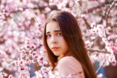 Çiçek açan kiraz ağacının yanında pembe çiçeklerle poz veren güzel kız. Bahar Parkı