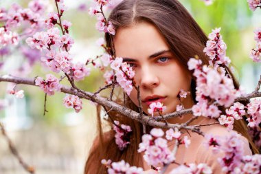 Güzel genç kız çiçek açan kiraz ağacının yanında beyaz çiçeklerle poz veriyor. Bahar geldi. 