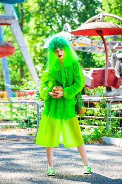 Güzel elbiseli genç bir kız eğlence parkının arka planında poz veriyor.