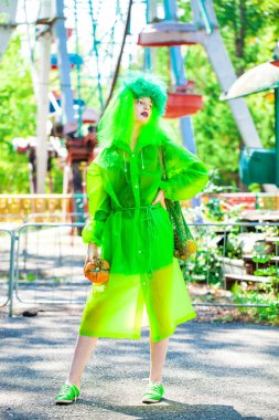 Güzel elbiseli genç bir kız eğlence parkının arka planında poz veriyor.