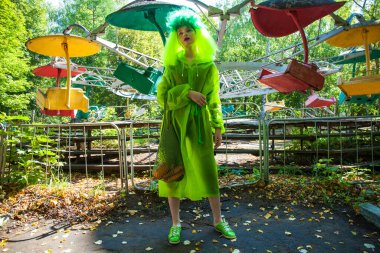 Güzel elbiseli genç bir kız eğlence parkının arka planında poz veriyor.