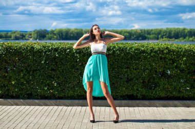 Uzun boylu, ince, turkuaz elbiseli, setin üzerinde poz veren güzel bir kızın portresi.