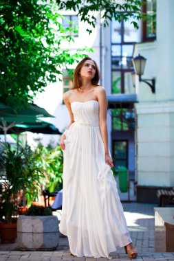 Uzun bacaklı, beyaz elbiseli, yaz caddesinde poz veren güzel bir kadın portresi.