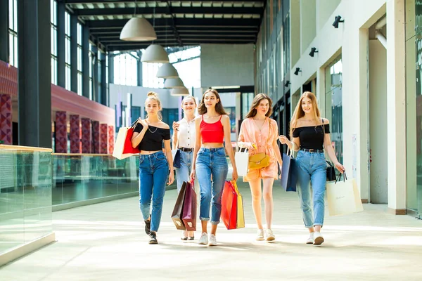 Kadın alışverişi. Arkaya bakan genç kızlar alışveriş merkezinde çantalarla yürüyorlar.