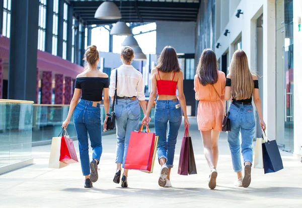 Kadın alışverişi. Arkaya bakan genç kızlar alışveriş merkezinde çantalarla yürüyorlar.
