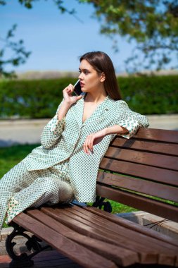 Genç, güzel esmer kadın parkta otururken poz veriyor.