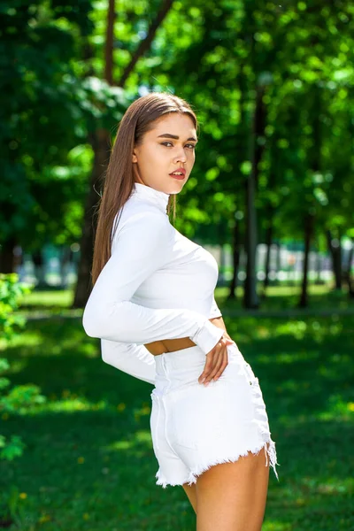 一个身穿白色粗斜纹棉布短裤的年轻漂亮姑娘在夏季公园摆姿势的画像 — 图库照片