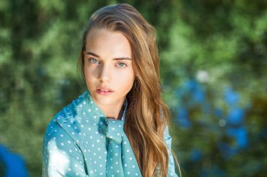 Turkuaz elbiseli genç bir kızın portresi. Bir yaz parkında gölün arka planında poz veriyor.