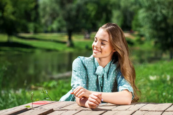 夏の公園の池を背景にポーズをとっているターコイズ色のドレスの若い美しい10代の女の子の肖像 — ストック写真