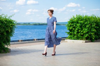 Mavi elbiseli güzel, esmer bir kadının tam boy portresi.