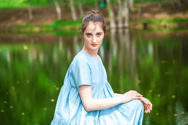 一个穿着郁郁葱葱的绿松石衣服的年轻漂亮女子在夏日公园池塘的背景下摆姿势的画像 — 图库照片