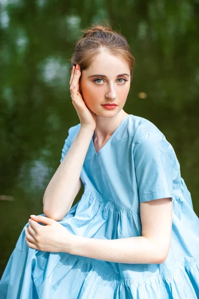 一个穿着郁郁葱葱的绿松石衣服的年轻漂亮女子在夏日公园池塘的背景下摆姿势的画像 — 图库照片
