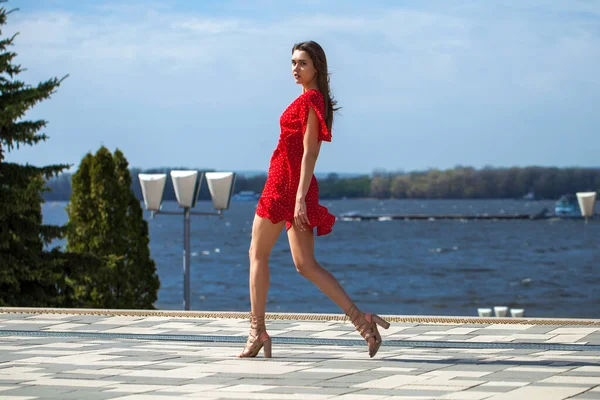 一位身穿红衣的年轻漂亮女子沿着堤岸散步时的全身像画像 — 图库照片