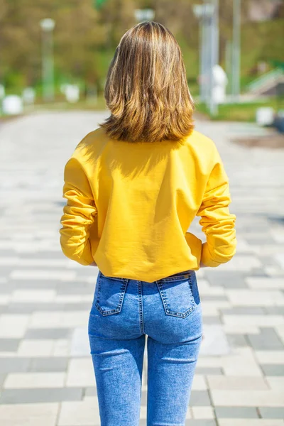 Arkadan bakıldığında, mavi kot pantolonlu sarışın manken, yaz parkı açık havada.