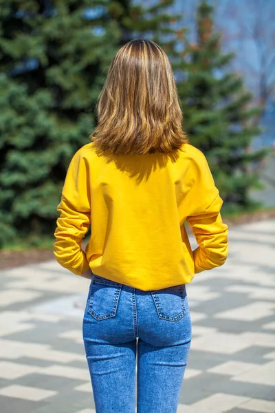 Arkadan bakıldığında, mavi kot pantolonlu sarışın manken, yaz parkı açık havada.