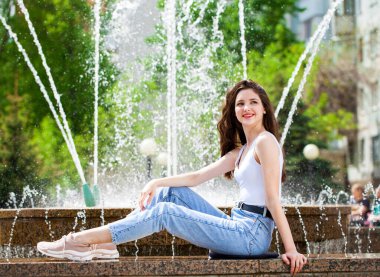 Bir şehir çeşmesinin arka planında poz veren güzel bir kızın tam boy portresi.