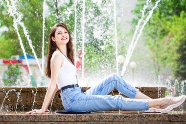 Bir şehir çeşmesinin arka planında poz veren güzel bir kızın tam boy portresi.