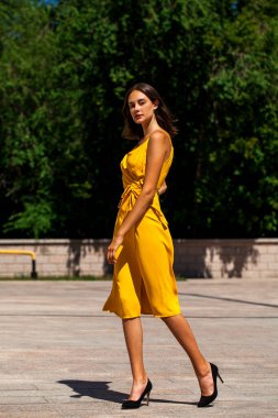 Açık yaz parkında, sarı elbiseli güzel bir kadının vücut portresi.