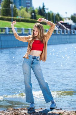 Uzun kollu ve mavi kotlu bej bluzlu genç bir kızın tam boy portresi.