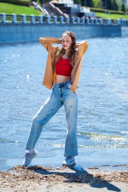 Uzun kollu ve mavi kotlu bej bluzlu genç bir kızın tam boy portresi.