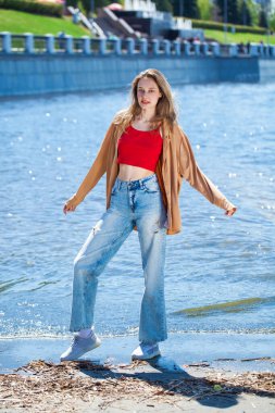 Uzun kollu ve mavi kotlu bej bluzlu genç bir kızın tam boy portresi.