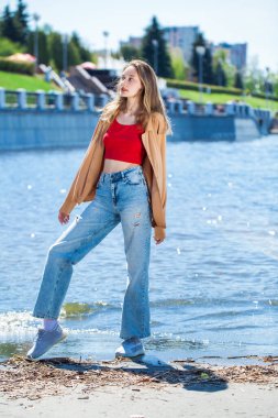 Uzun kollu ve mavi kotlu bej bluzlu genç bir kızın tam boy portresi.