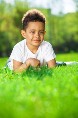 Beş yaşındaki küçük çocuk bir yaz parkında yeşil çimlerin üzerinde yatıyor.