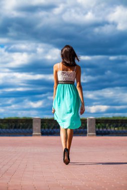 Tam boy portre. Turkuaz elbiseli genç ve güzel bir kız sette yürüyor.
