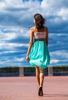 Tam boy portre. Turkuaz elbiseli genç ve güzel bir kız sette yürüyor.