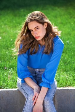 Mavi bluzlu ve gri kotlu güzel esmer kız, açık hava yaz parkı. 