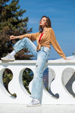 Uzun kollu ve mavi kotlu bej bluzlu genç bir kızın tam boy portresi.