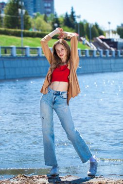 Uzun kollu ve mavi kotlu bej bluzlu genç bir kızın tam boy portresi.