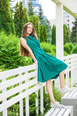 Yeşil elbiseli ve siyah benekli spor ayakkabılı genç bir kızın tam boy portresi.