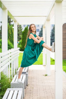 Yeşil elbiseli ve siyah benekli spor ayakkabılı genç bir kızın tam boy portresi.