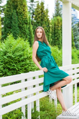 Yeşil elbiseli ve siyah benekli spor ayakkabılı genç bir kızın tam boy portresi.