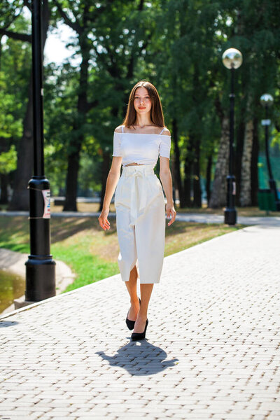 Портрет в полный рост, молодая красивая девушка в белой юбке, позирующая в летнем парке