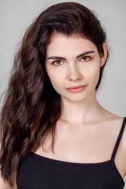 Gri arka planda izole edilmiş güzel esmer bir kızın yakın portresi.