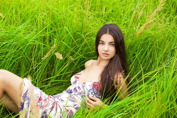 Mladá žena odpočívá a den vleže na zelené trávě — Stock fotografie