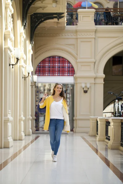 Junge Frau in gelbem Mantel läuft durch den Laden — Stockfoto