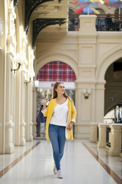 Mujer joven con abrigo amarillo caminando en la tienda —  Fotos de Stock