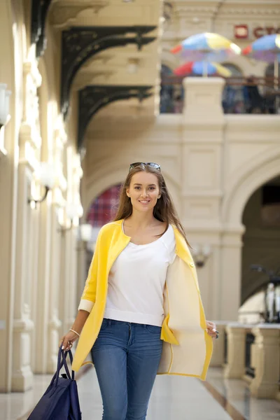 Mujer joven con abrigo amarillo caminando en la tienda — Foto de Stock