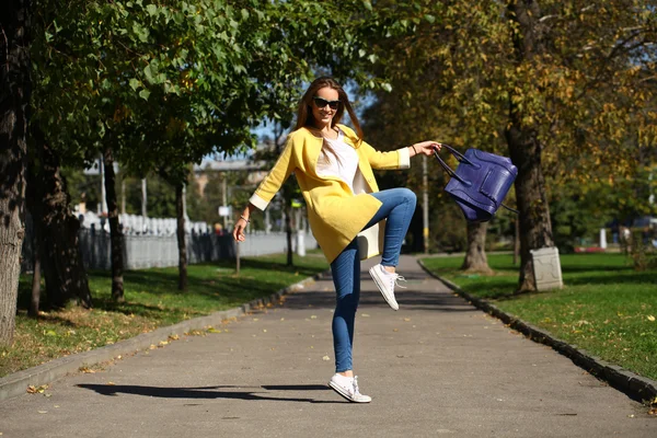 Glückliche Frau in gelbem Mantel spaziert durch die Herbststraße — Stockfoto