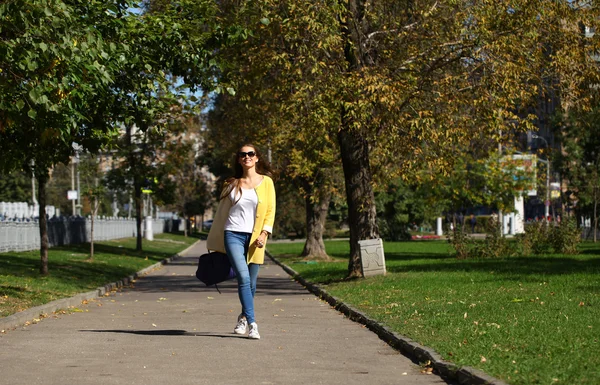 Щаслива жінка в жовтому пальто, що йде осінньою вулицею — стокове фото