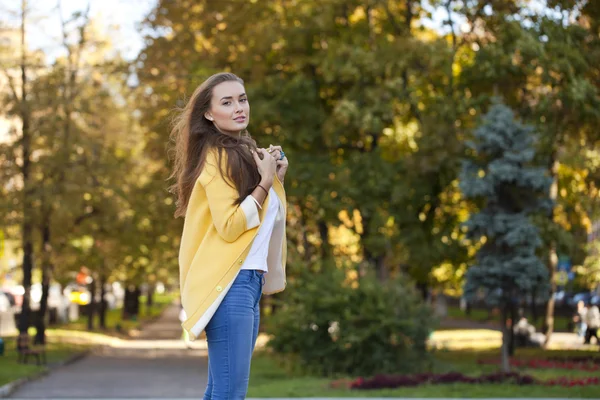 幸福的年轻女人在黄色的外套，在秋季街头 — 图库照片