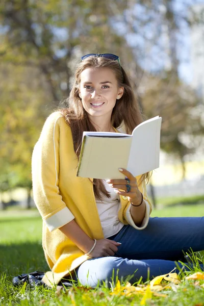 Sonbahar parkta oturan ve bir kitap okuma güzel kız öğrenci — Stok fotoğraf